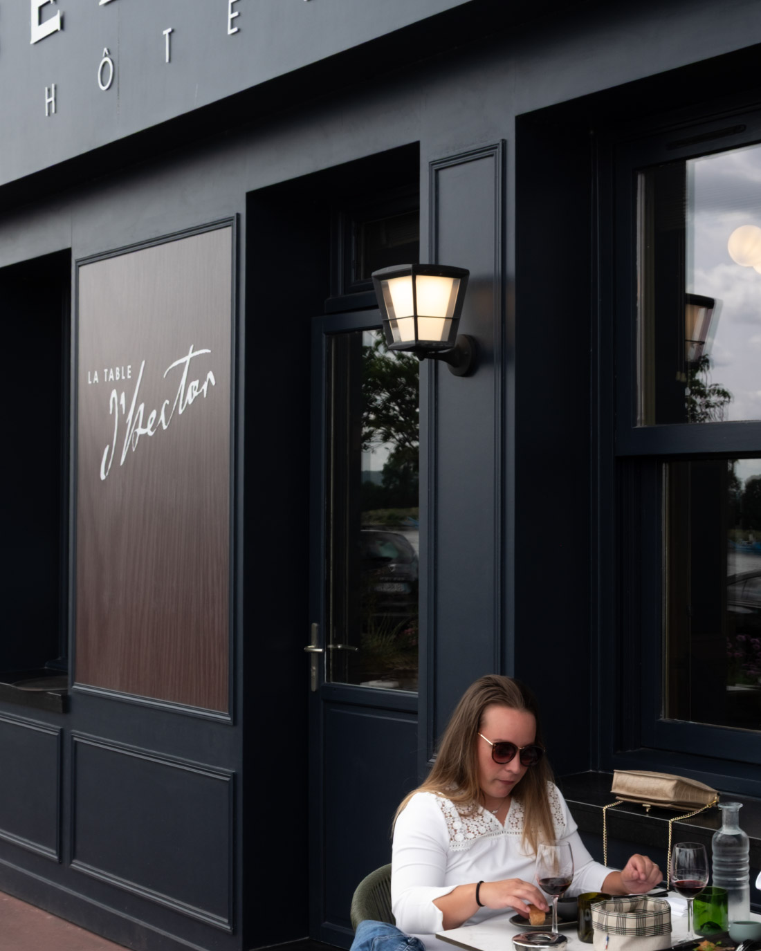 Femme déjeunant en terrasse devant la façade et l’enseigne du restaurant La Table d’Hector à La Bouille